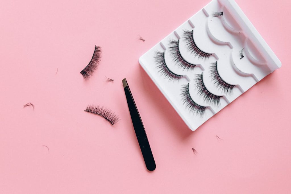 Stylish arrangement of false eyelashes and tweezers on a pink background, perfect for beauty themes.